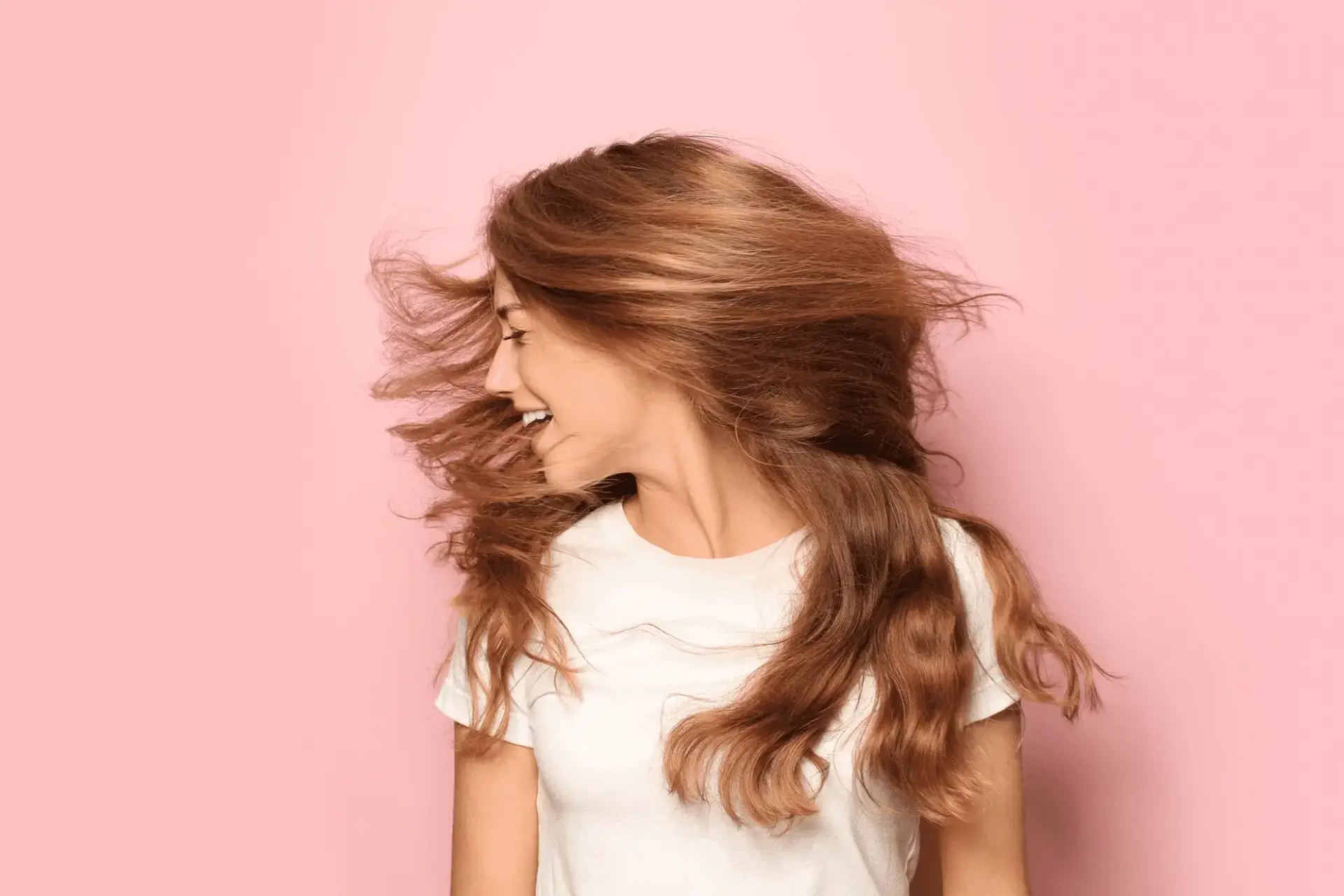 A female with red hair shaking her long hair on a pink background